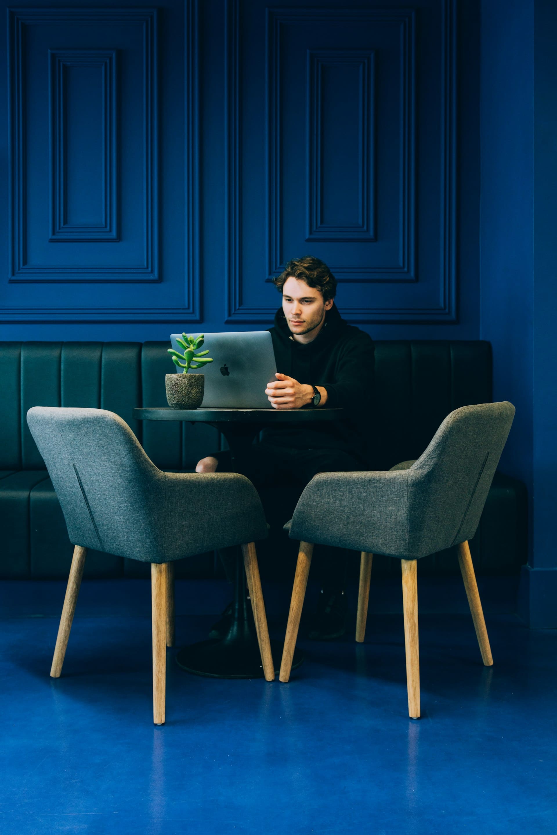 A man works on a laptop at a round table with two chairs in a modern, blue-themed space